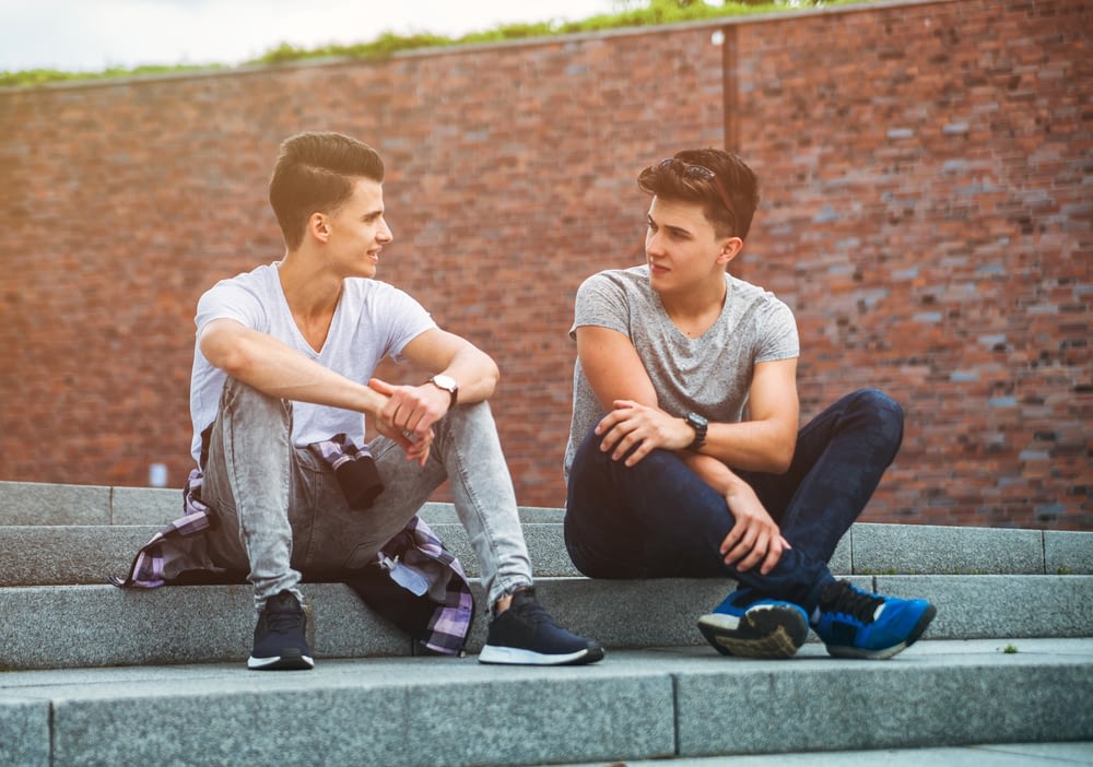 Two friends casual wear sitting on stairs in town and talking, best friend